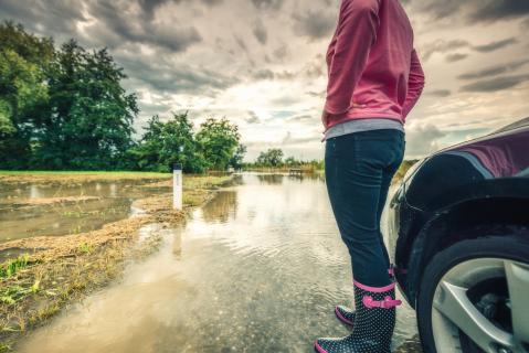 Frau steht an Auto auf überfluteter Straße