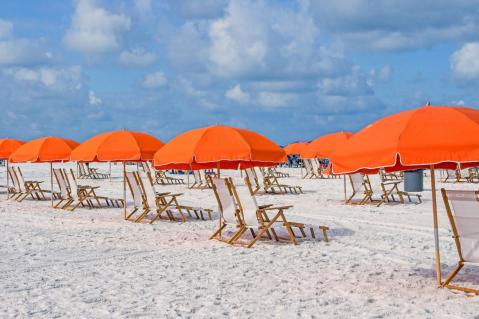 Orangefarbene Sonnenschirme stehen mit Liegestühlen am Strand