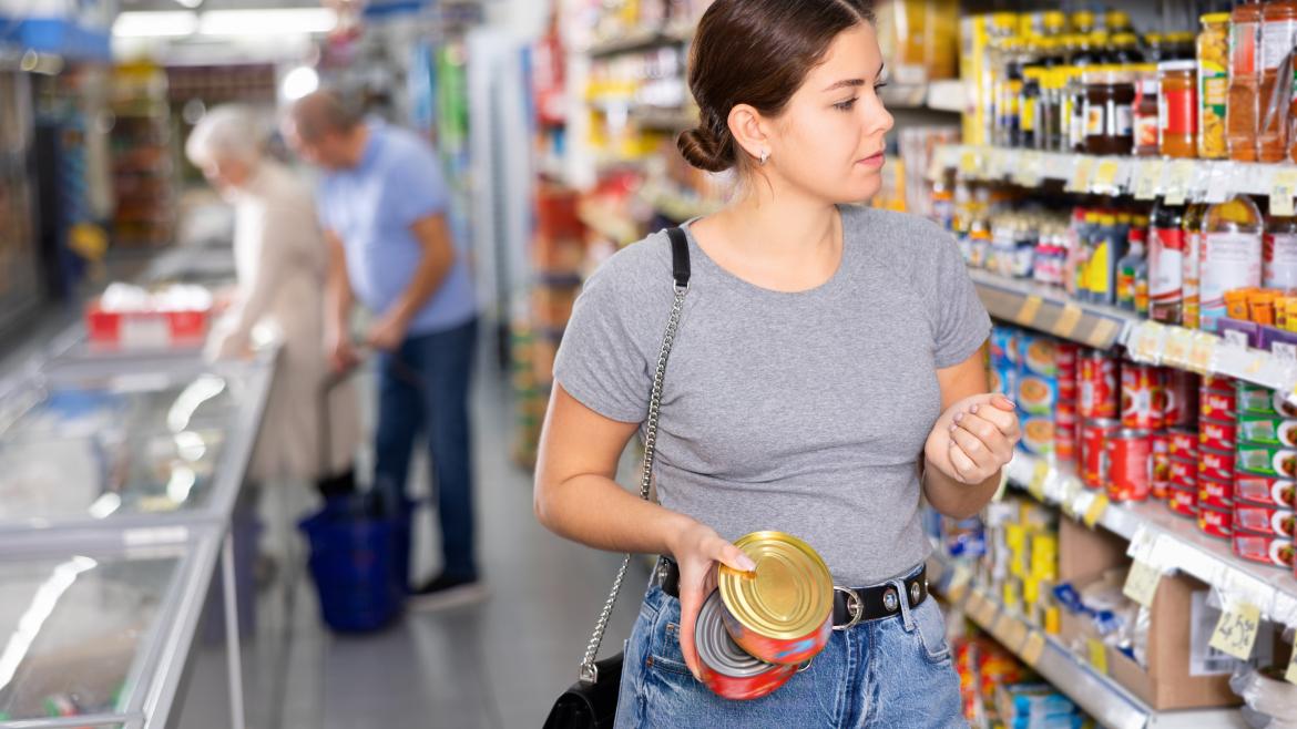 Junge Frau im Supermarkt mit Konservendosen in der Hand