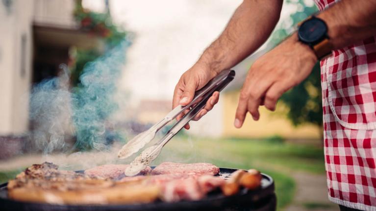 Person mit kariertem Hemd grillt Wurst